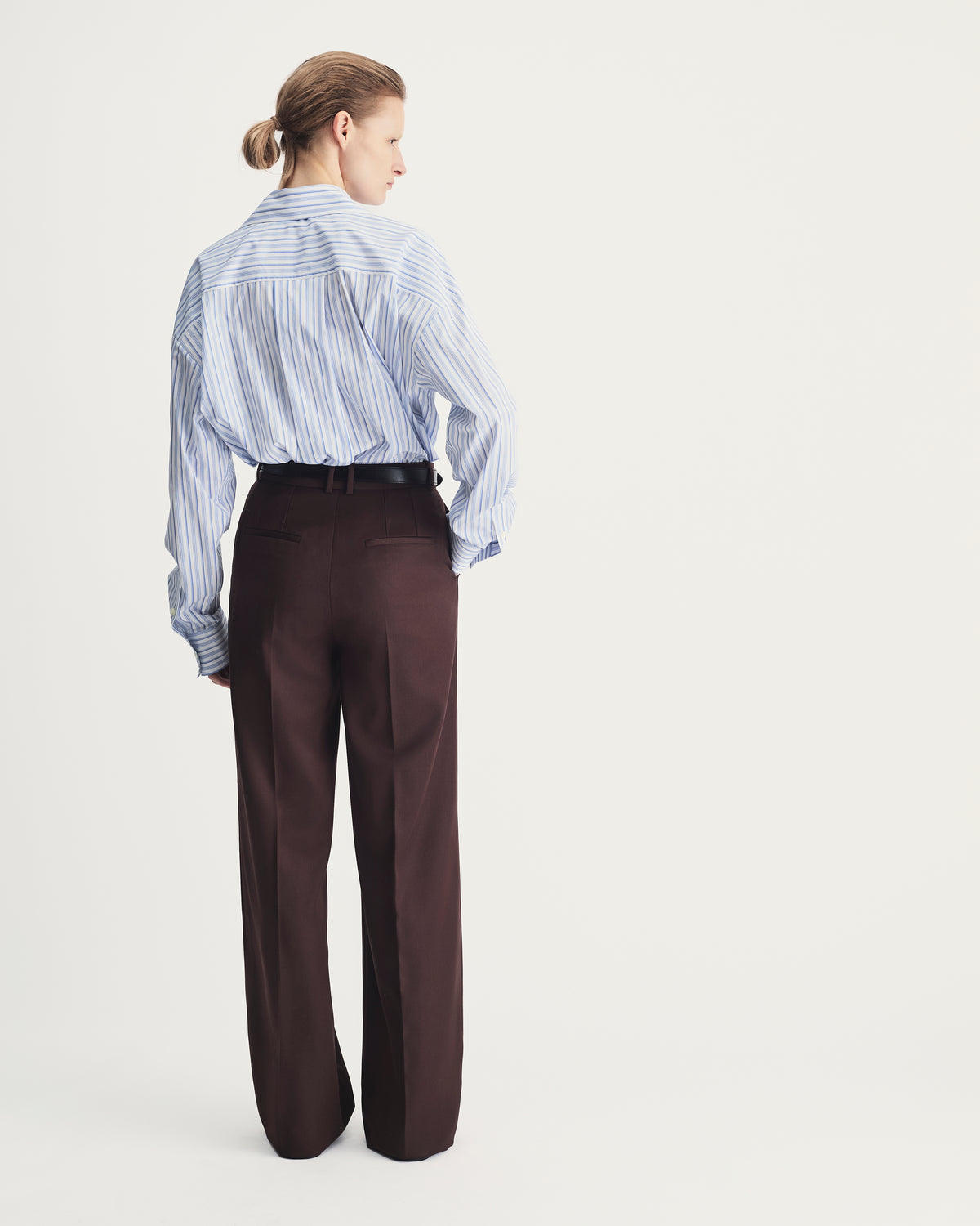 Person wearing a blue striped shirt and brown pants on a white background
