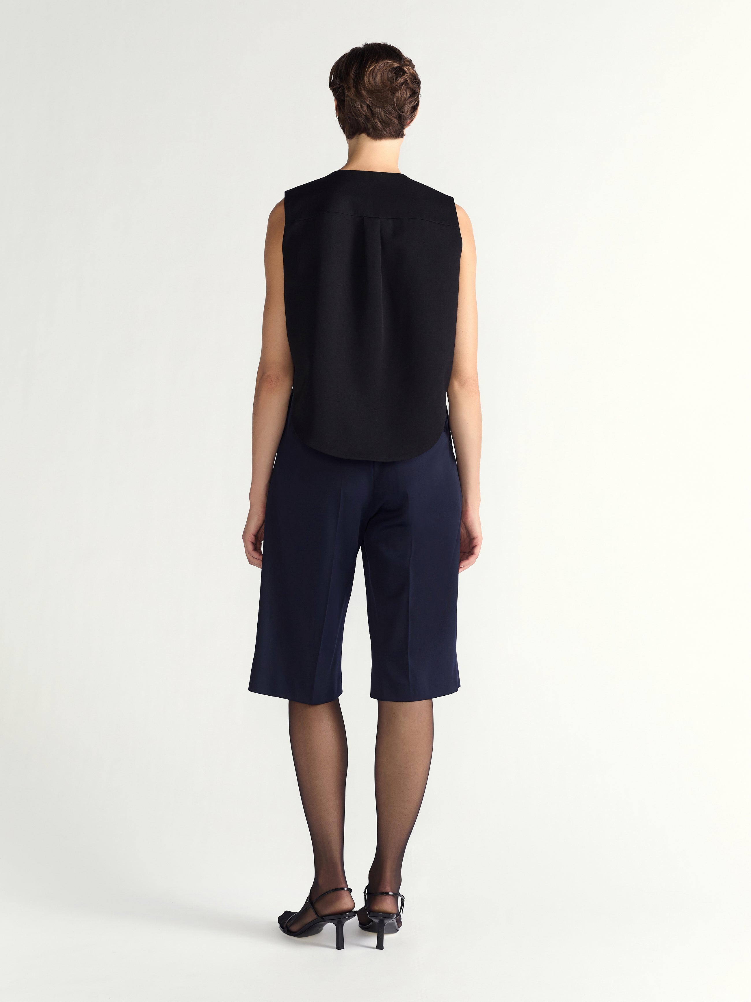 Person wearing a black sleeveless top and navy blue shorts on a white background