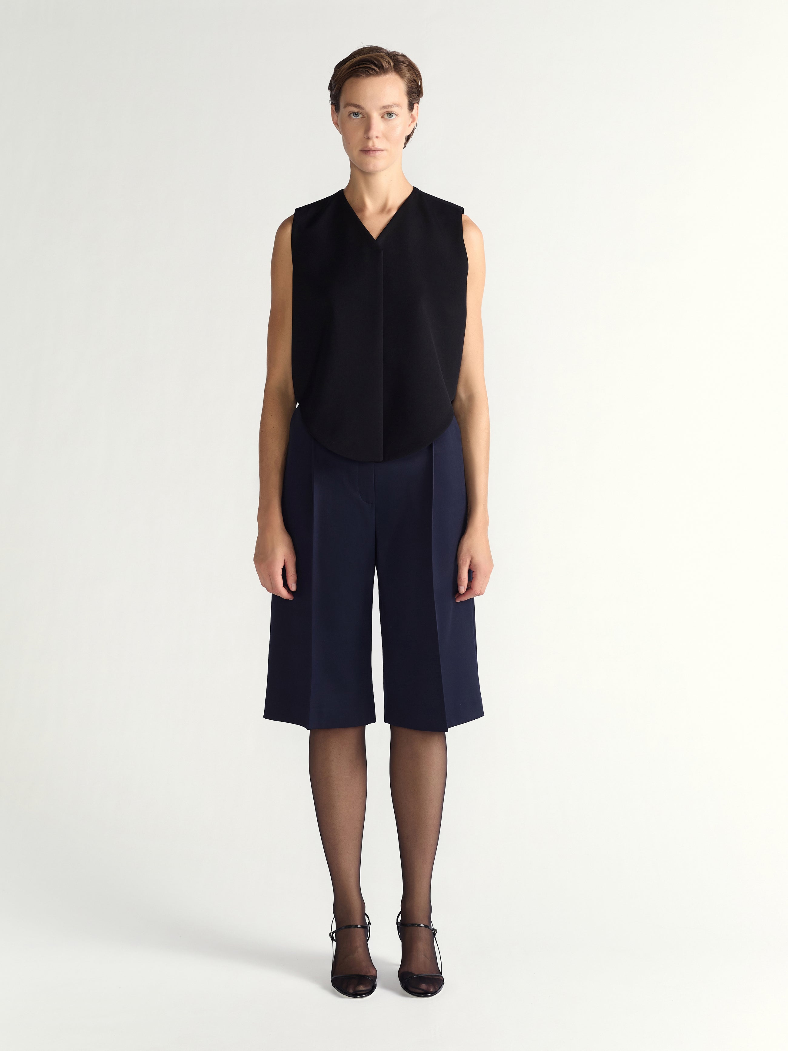 Person wearing a black sleeveless top and navy blue shorts on a white background