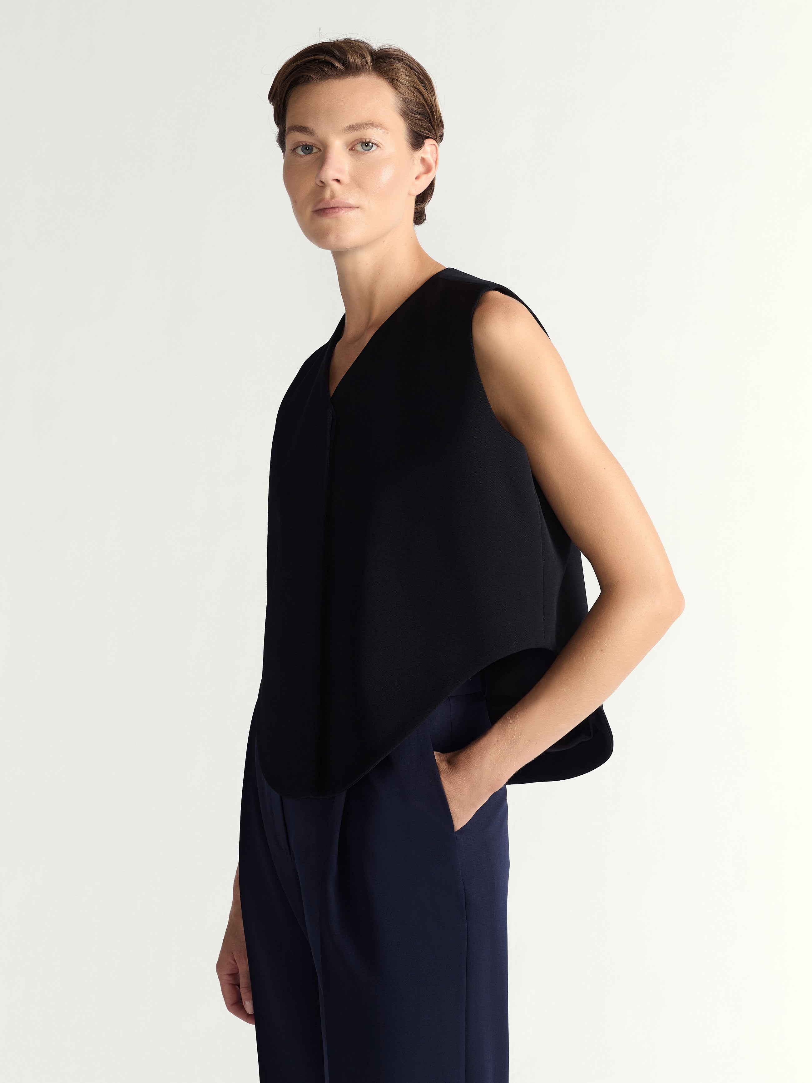 Person wearing a black sleeveless top and dark pants on a light gray background