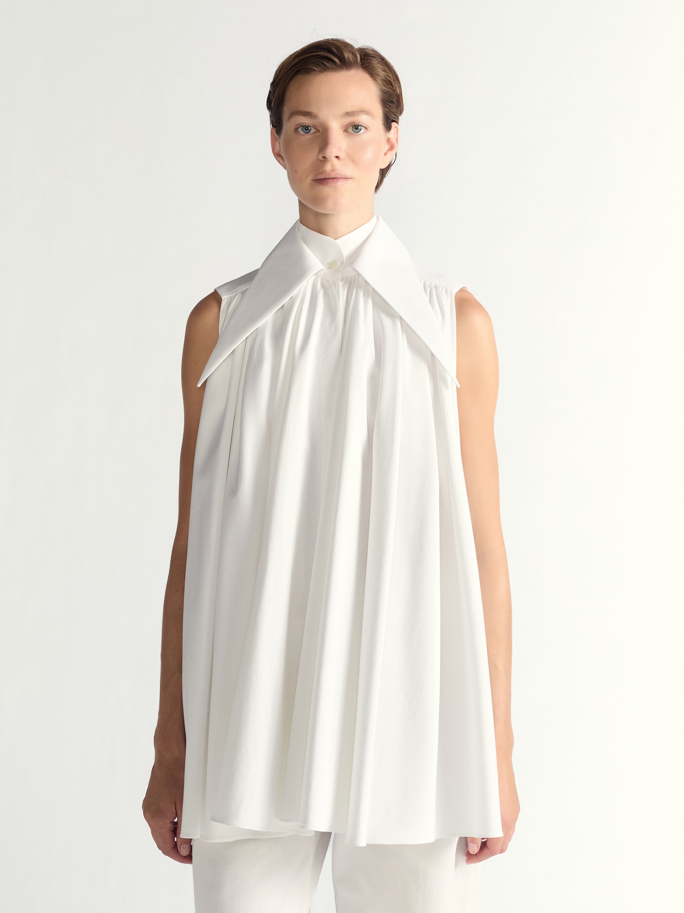 Person wearing a white sleeveless dress with a high collar on a plain background