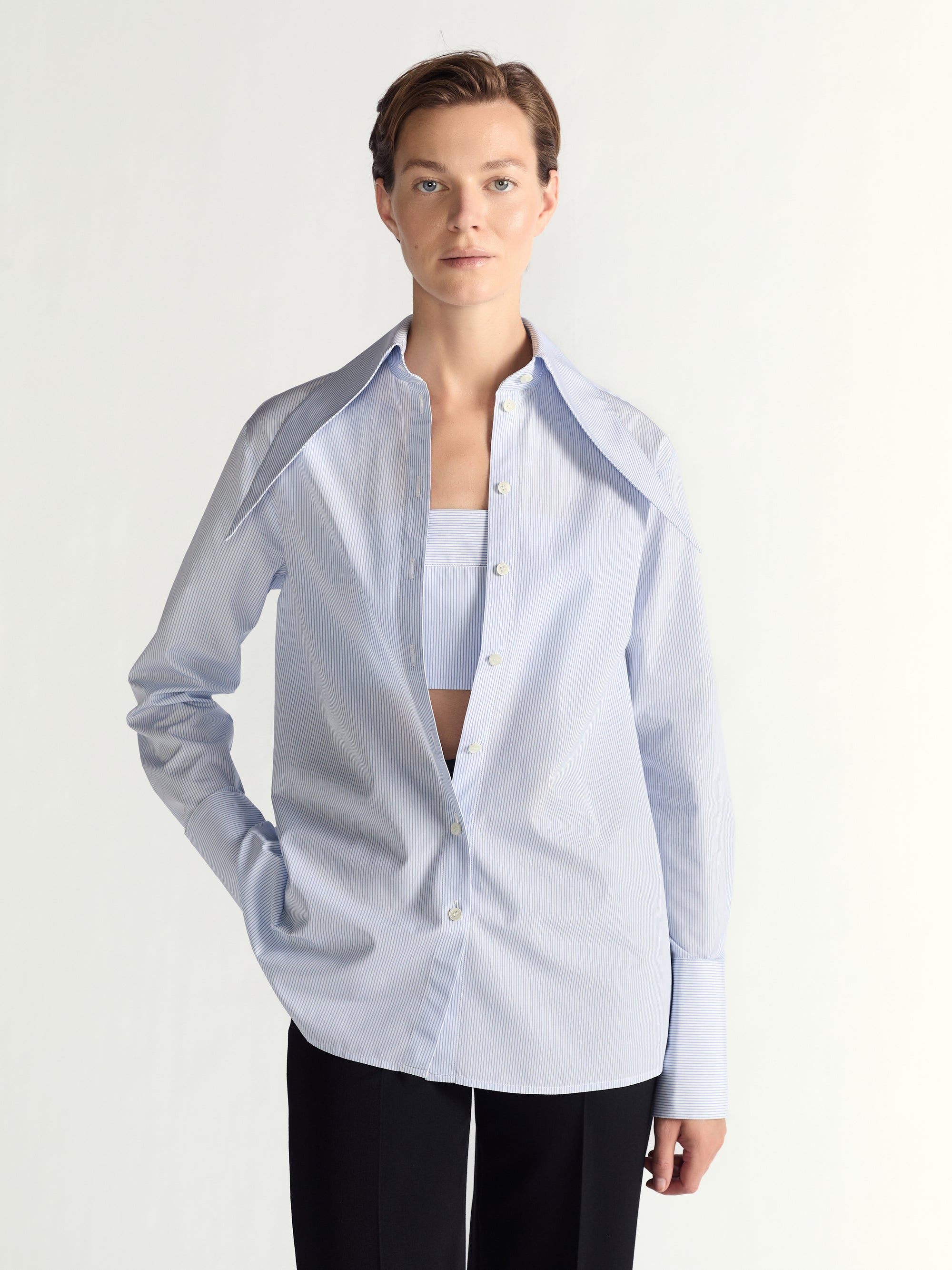 Person wearing a light blue button-up shirt over a blue top with black pants on a plain background