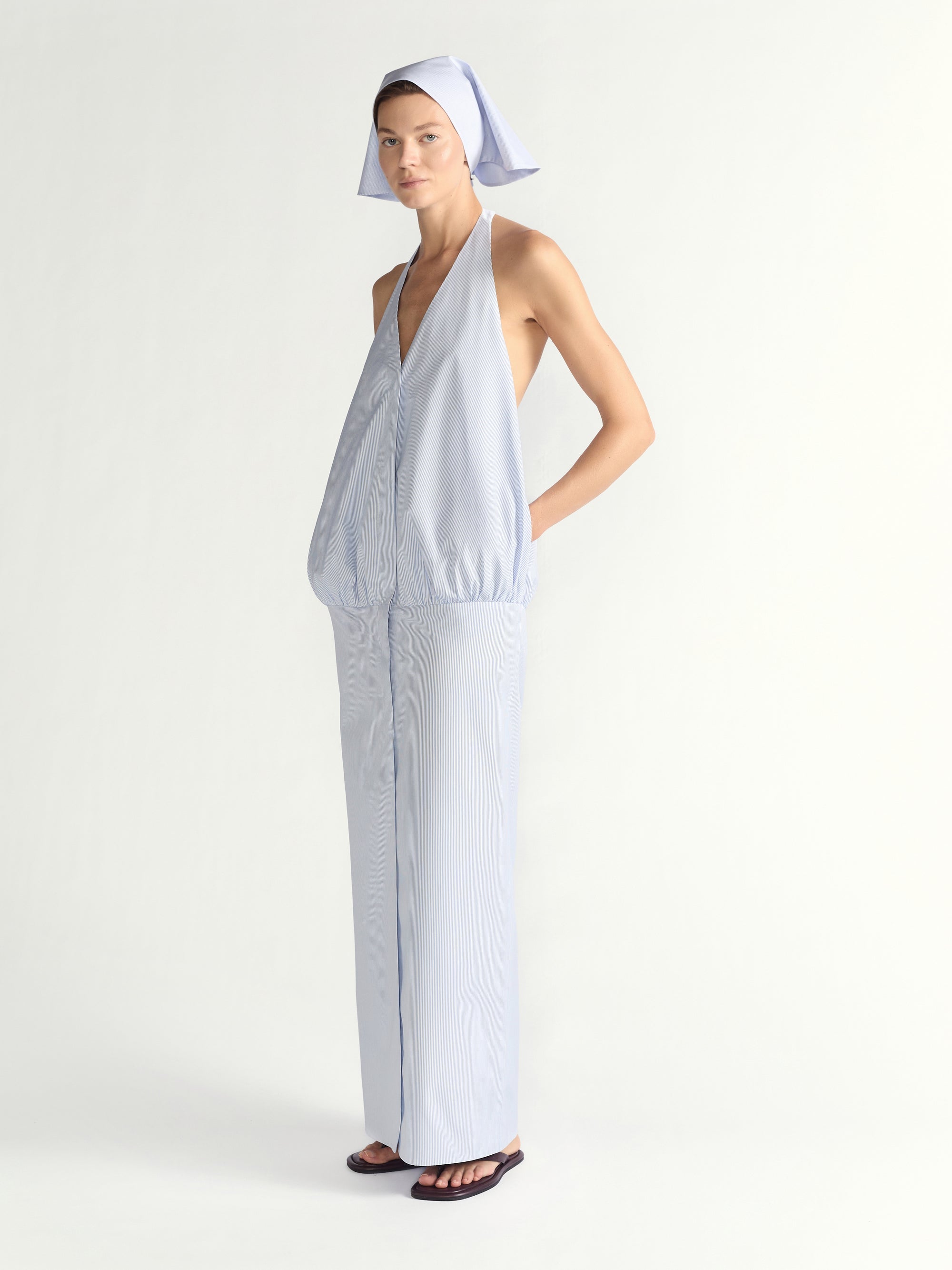 Woman wearing a blue halter dress with a headscarf on a plain background