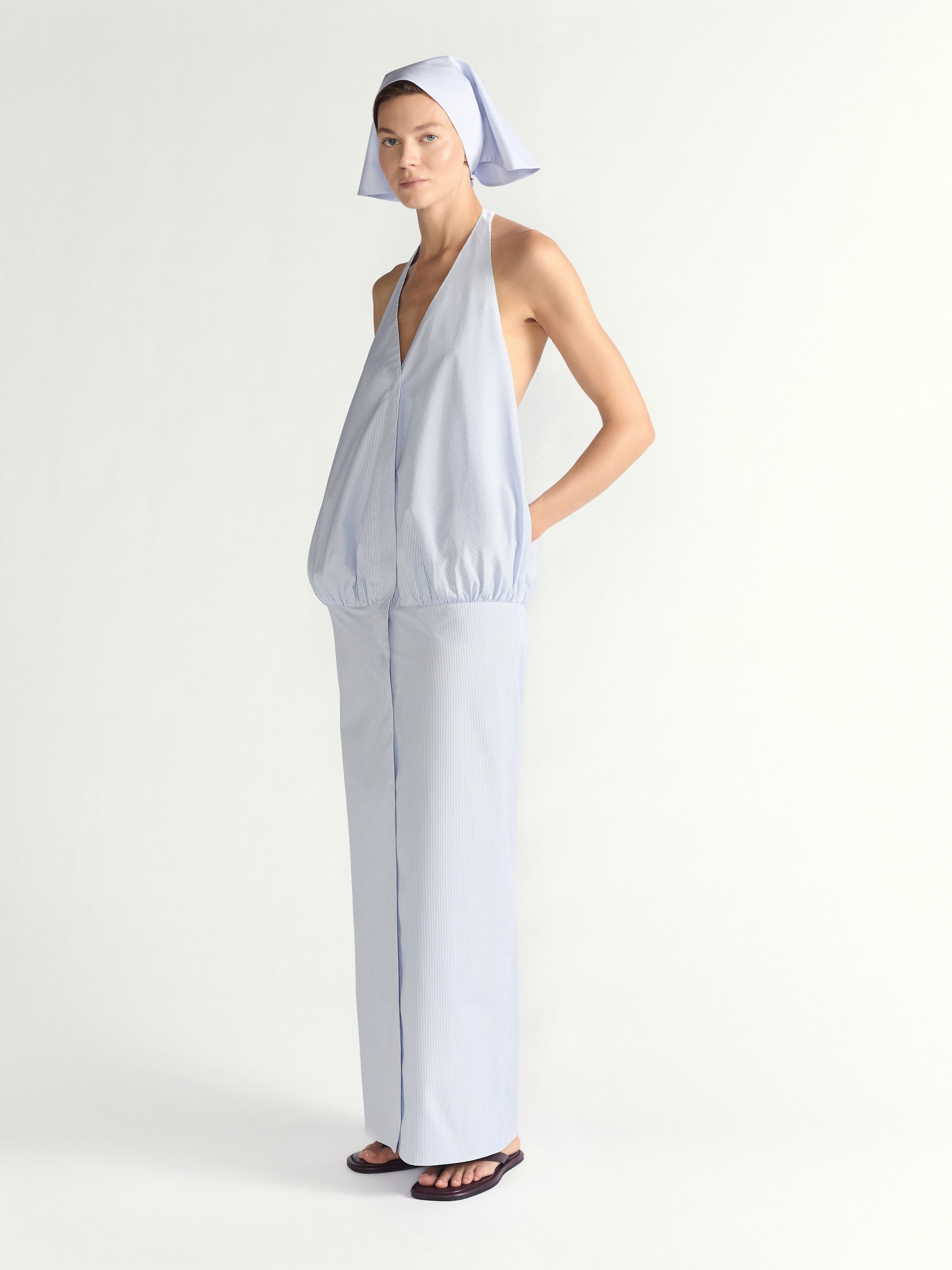 Woman wearing a blue halter dress with a headscarf on a plain background