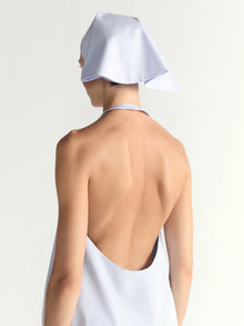 Person wearing a blue dress and a white headscarf on a light gray background