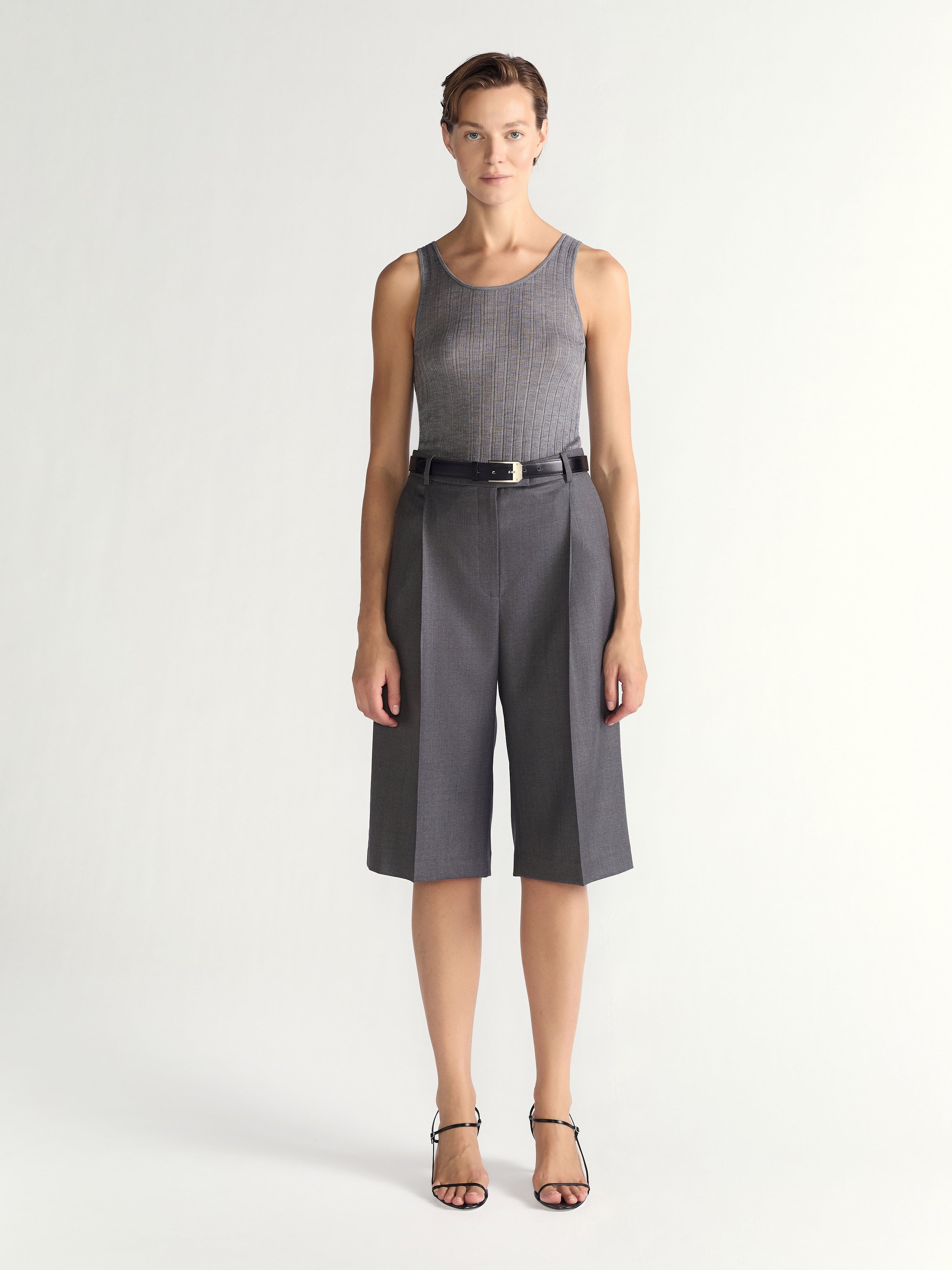 Woman wearing a sleeveless gray top and gray shorts on a white background