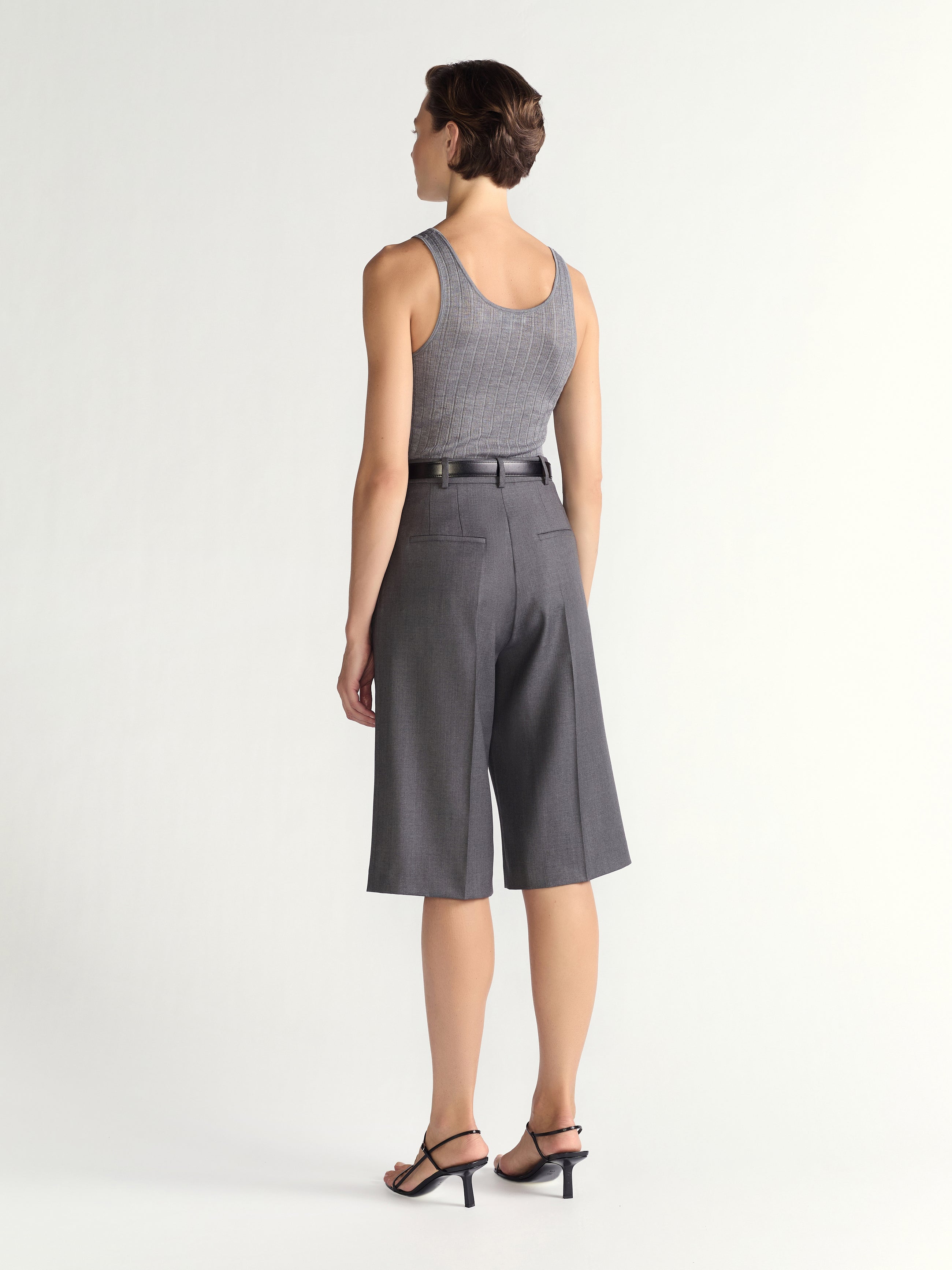 Woman wearing a gray sleeveless top and high-waisted shorts on a white background