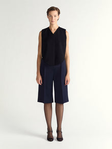 Person wearing a black sleeveless top and navy blue shorts on a white background