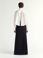 Person wearing a white blouse with a sheer back panel and a long black skirt on a white background