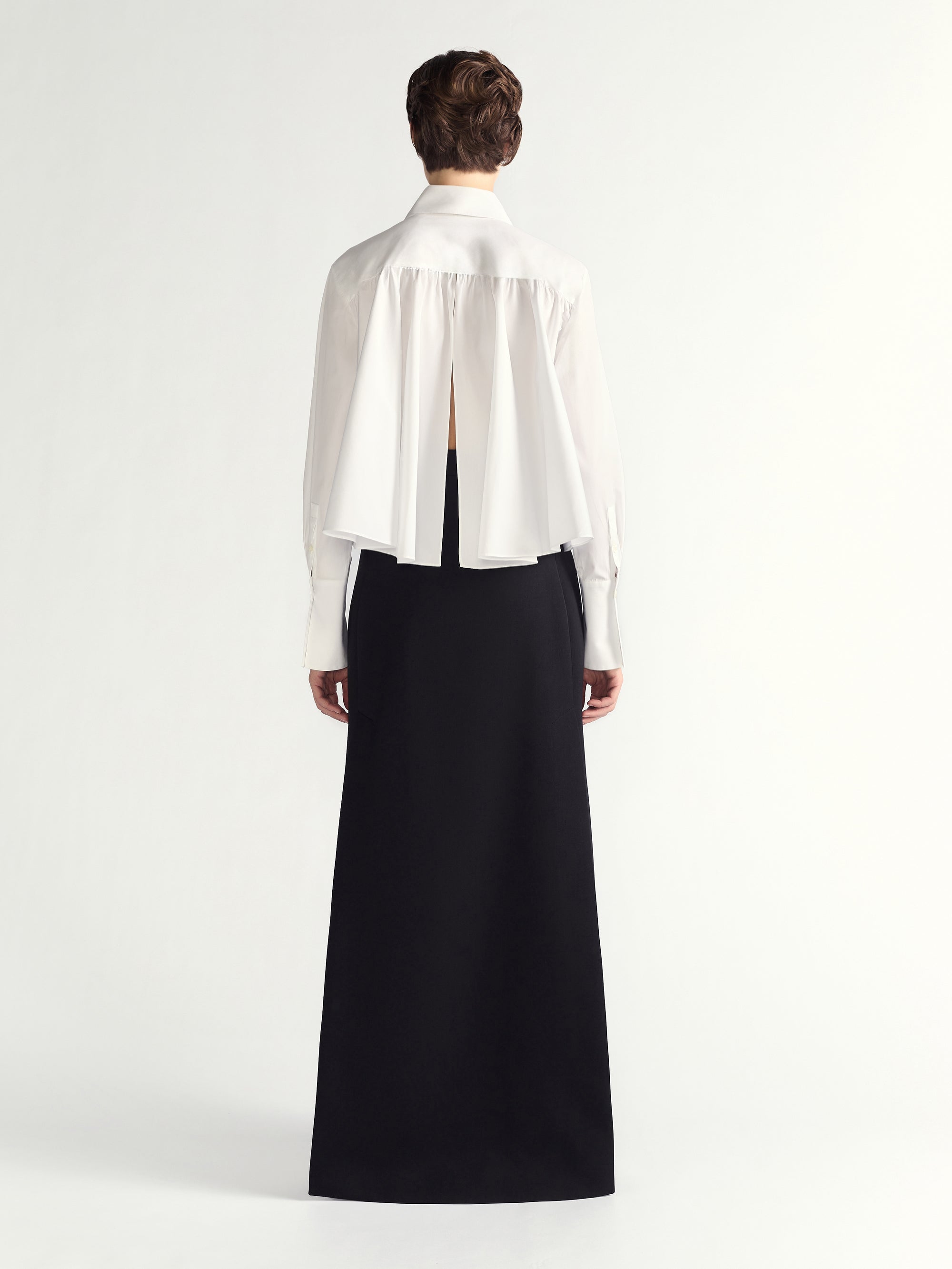 Person wearing a white blouse with a sheer back panel and a long black skirt on a white background