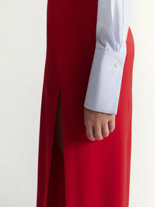 Person wearing a red skirt and white shirt with blue striped cuffs against a white background