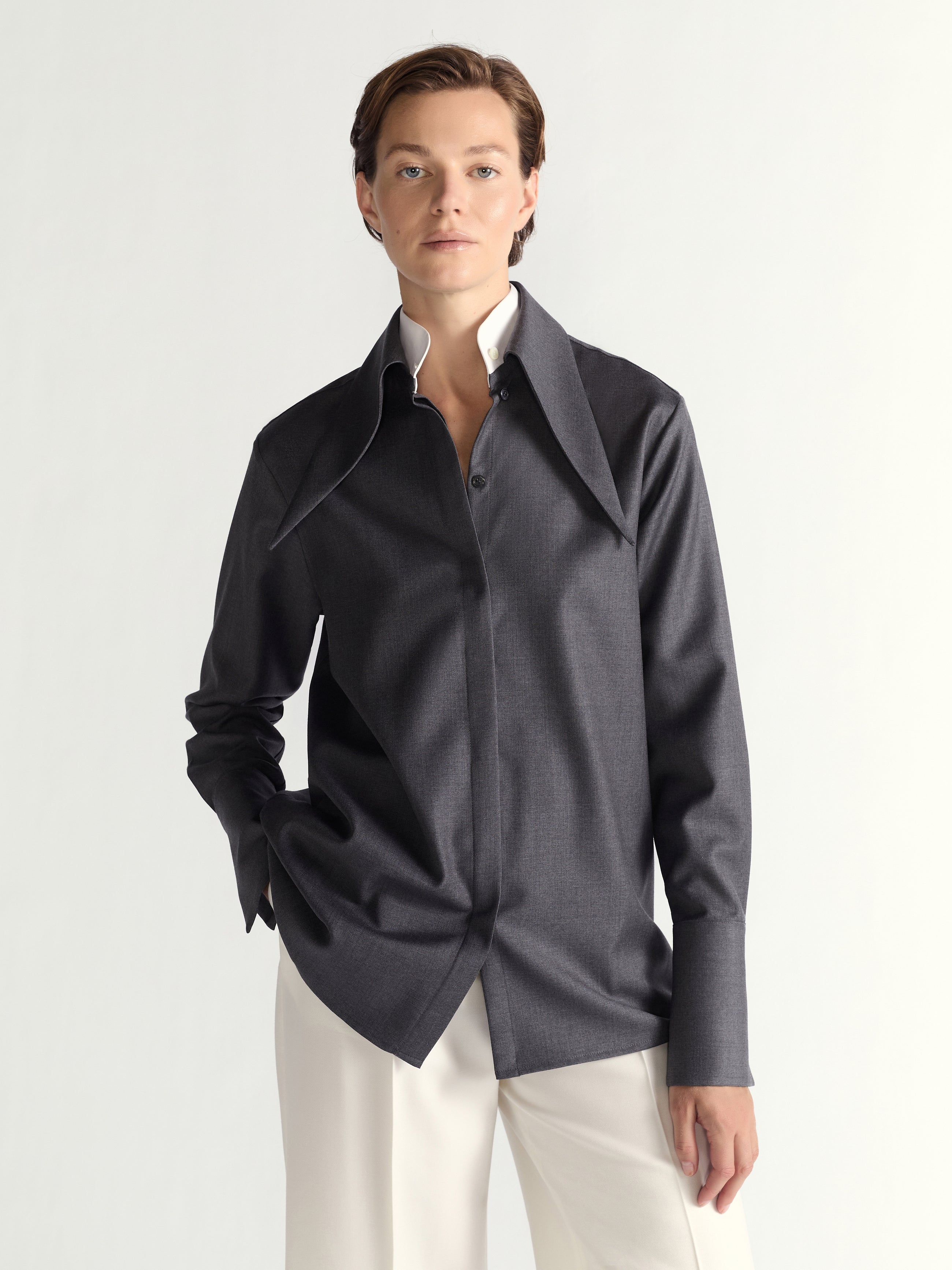 Person wearing a dark gray shirt with a  light-colored pants on a plain background