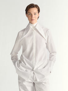 Person wearing a white dress shirt with a high collar on a plain background