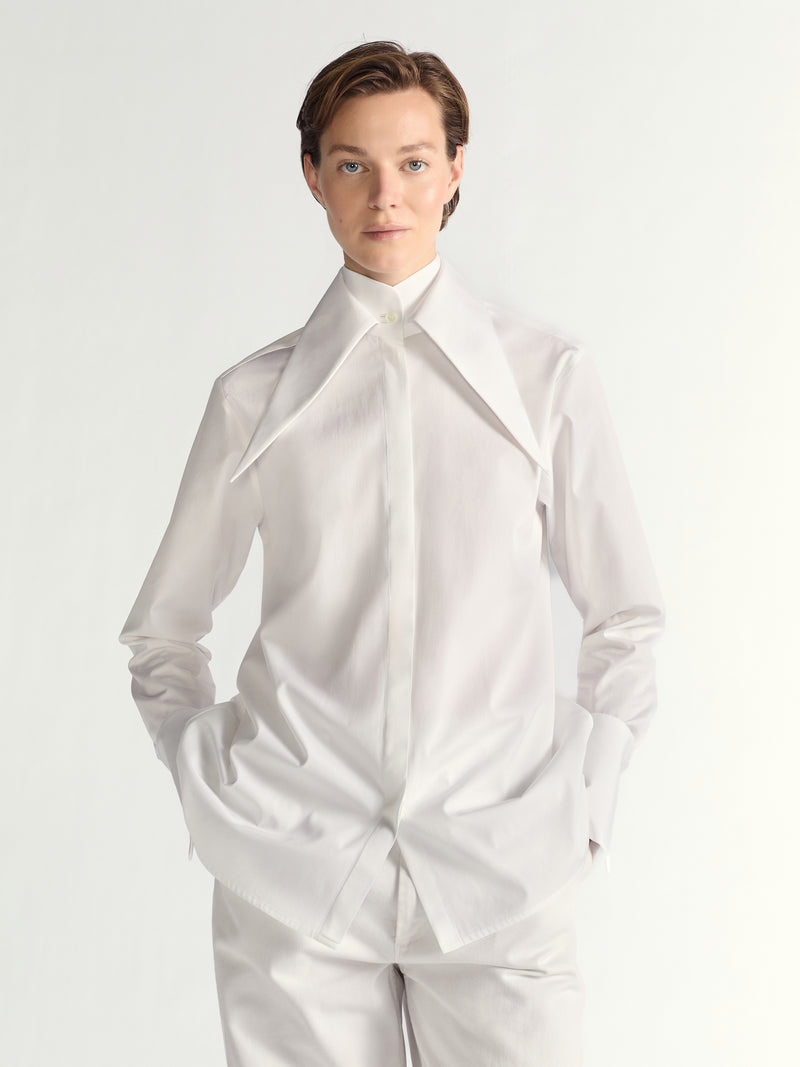 Person wearing a white dress shirt with a high collar on a plain background