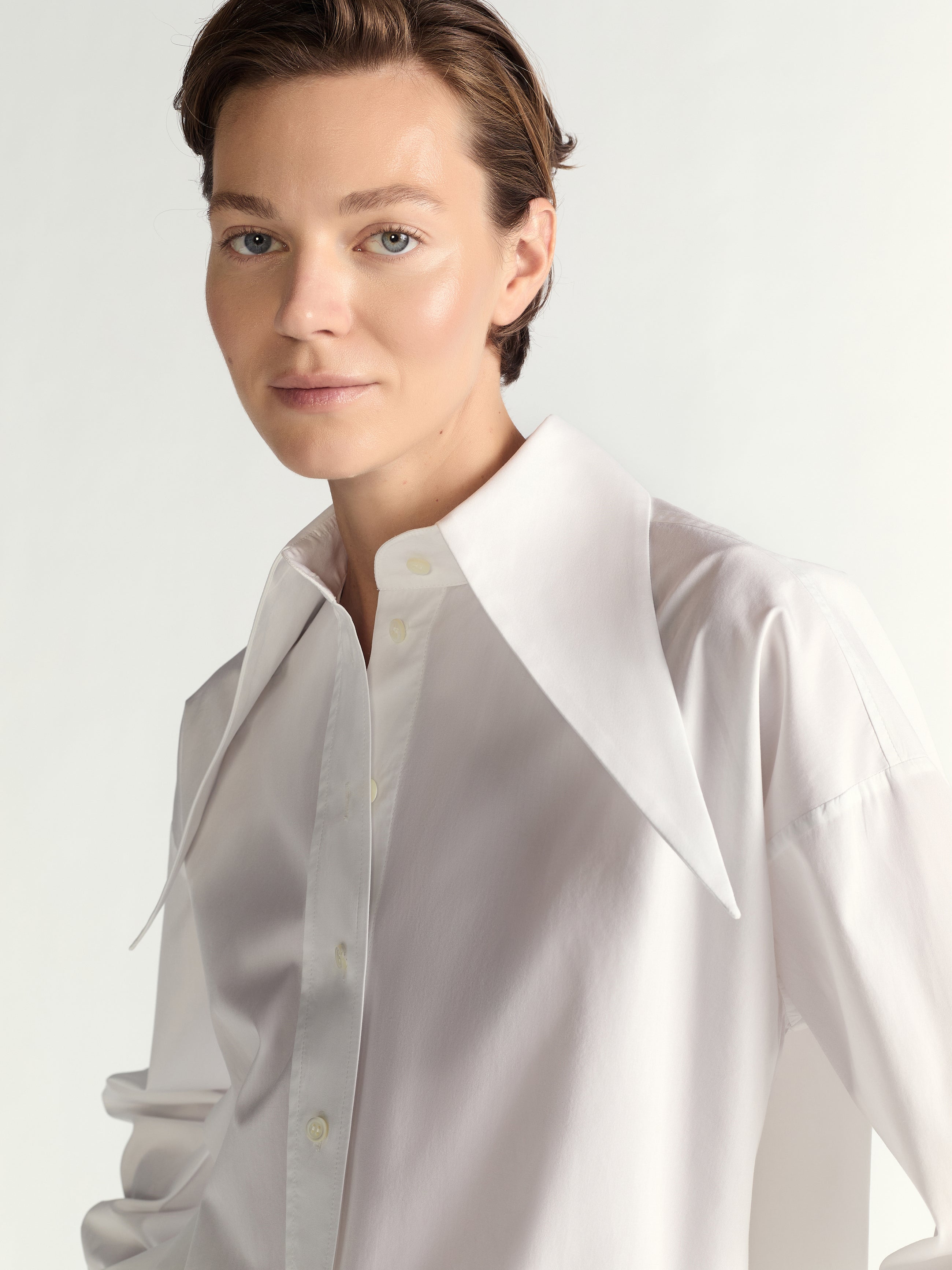 Person wearing a whiite shirt with a white collar against a plain background
