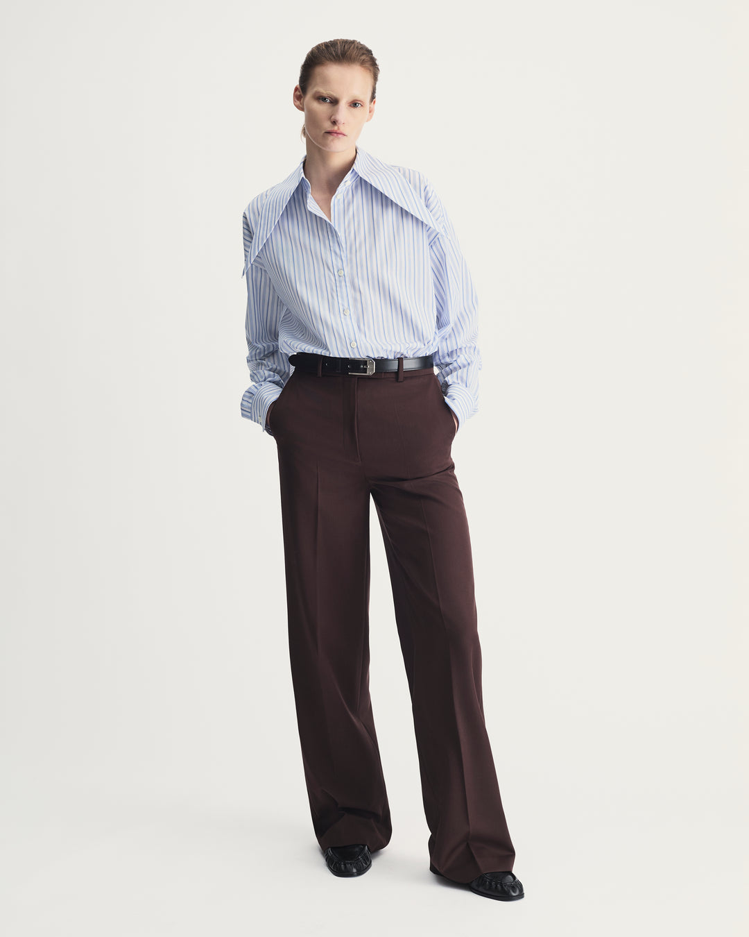 Person wearing a striped shirt and brown pants on a white background