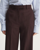 Brown pleated pants worn with a blue and white striped shirt on a light gray background