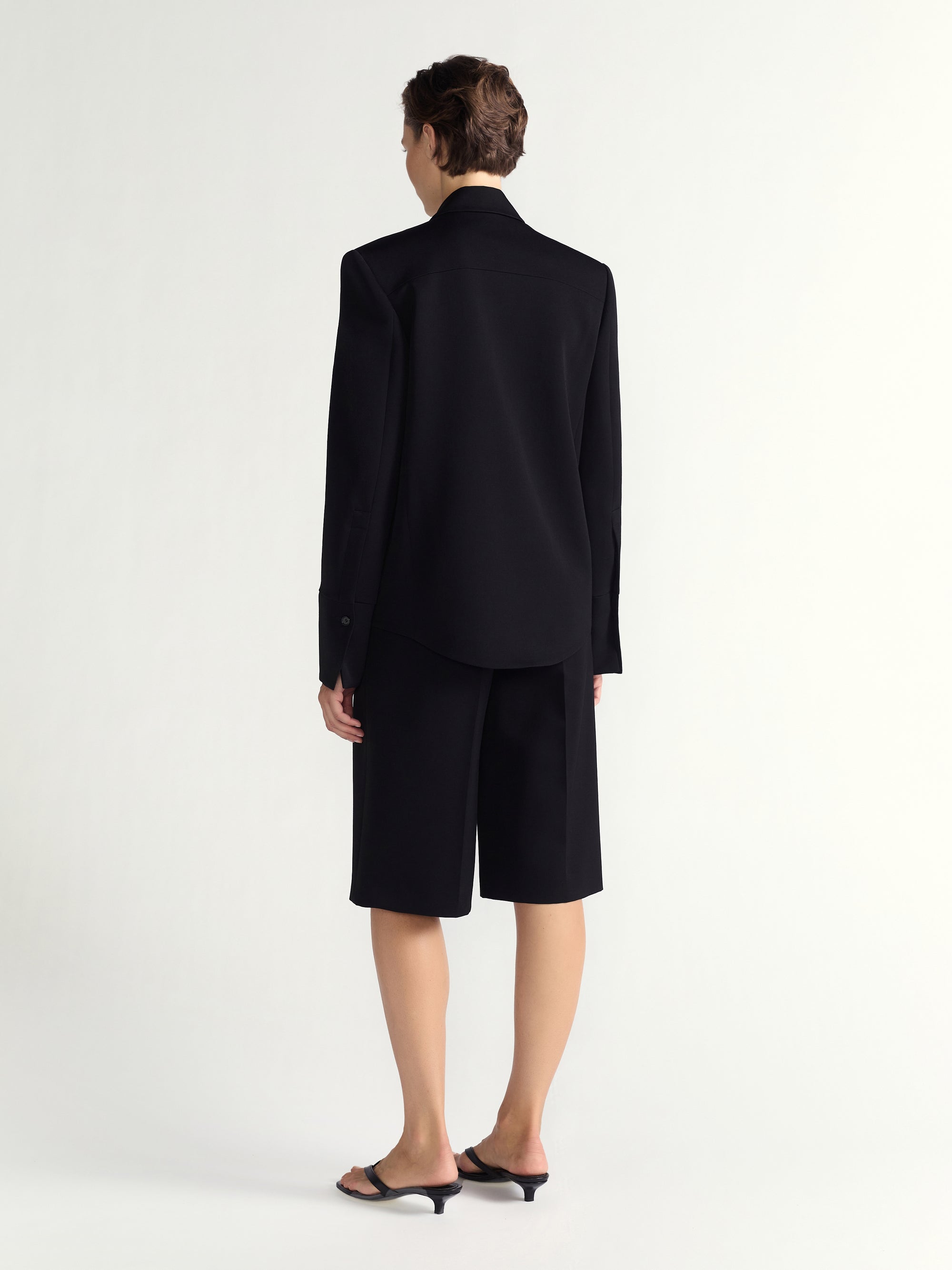 Person wearing a black suit with a jacket and shorts on a white background