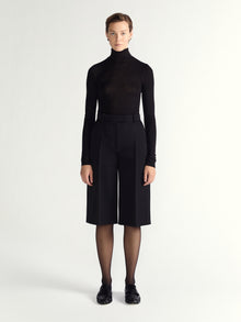 Person wearing a black turtleneck and black high-waisted shorts on a white background