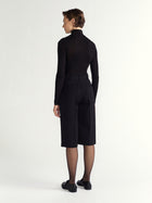 Person wearing a black outfit with a high collar and black shoes on a white background