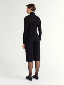 Person wearing a black outfit with a high collar and black shoes on a white background