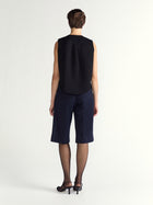 Person wearing a black sleeveless top and navy blue shorts on a white background