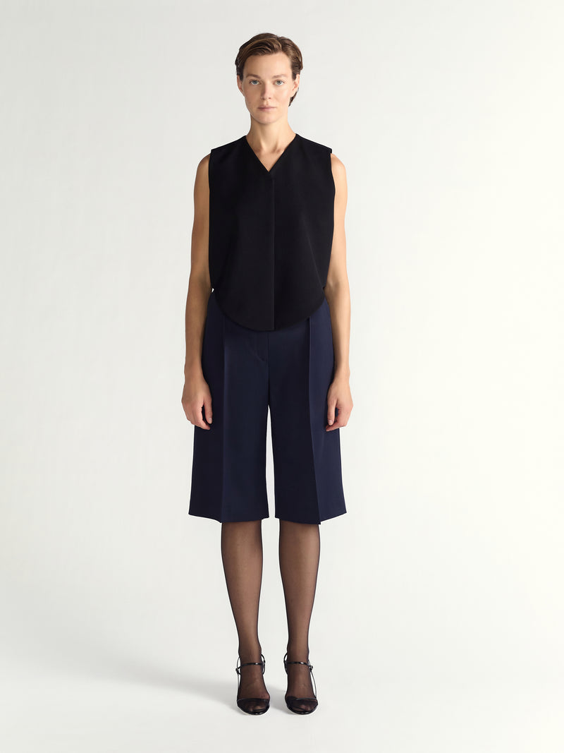 Person wearing a black sleeveless top and navy blue shorts on a white background