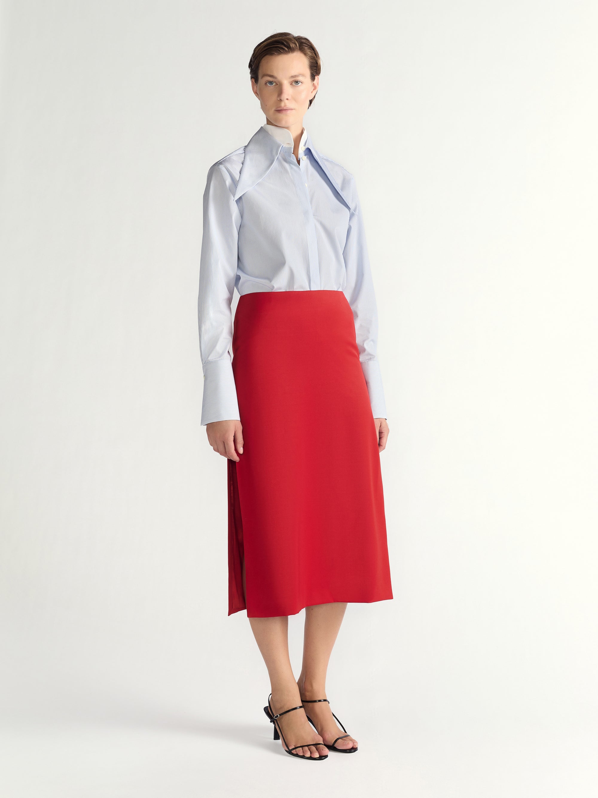 Woman wearing a white shirt with a blue collar and a red skirt on a light gray background