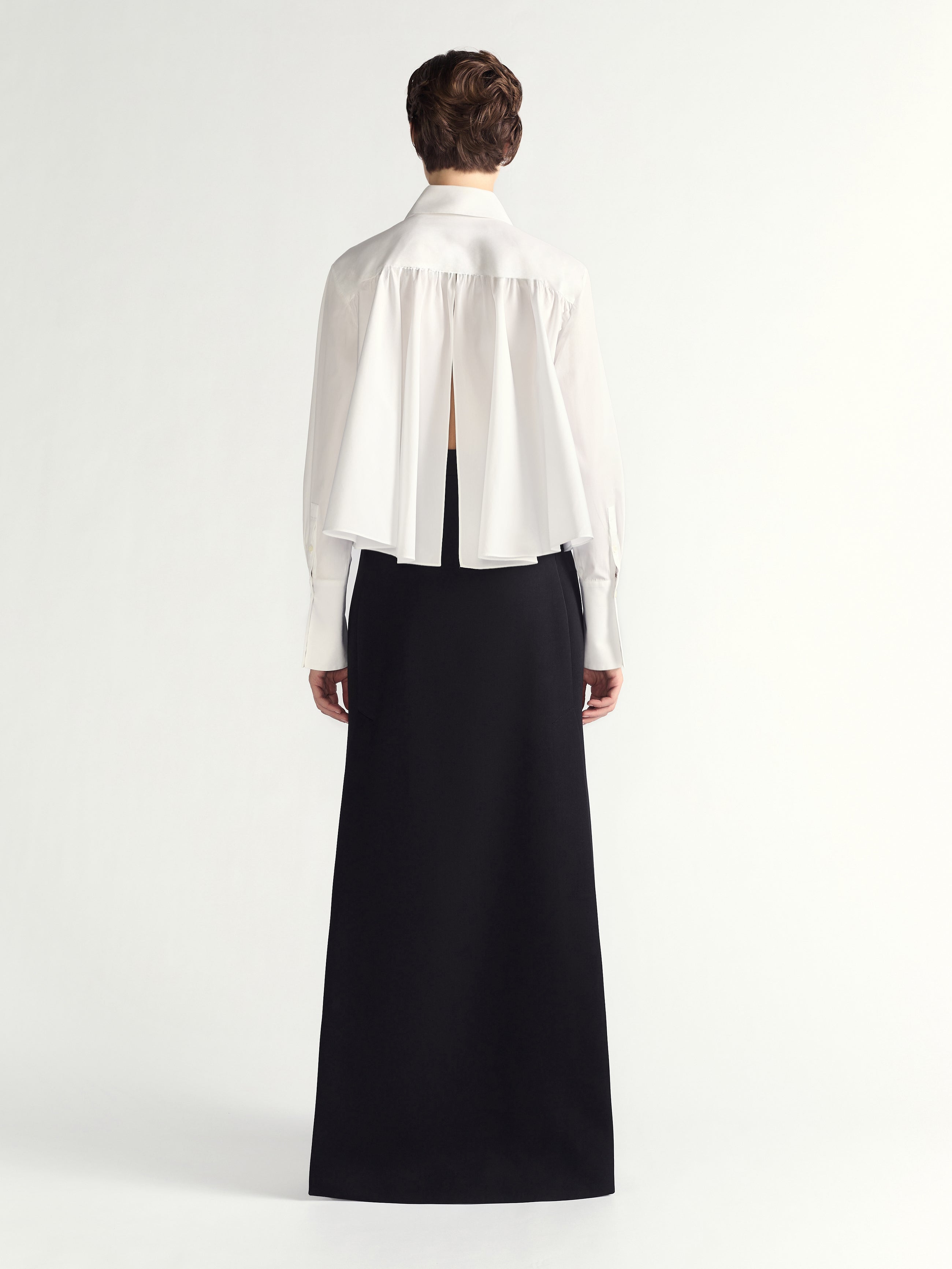 Person wearing a white blouse with a sheer back panel and a long black skirt on a white background