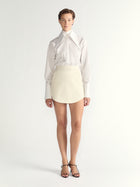 Person wearing a white blouse and cream skirt on a plain background