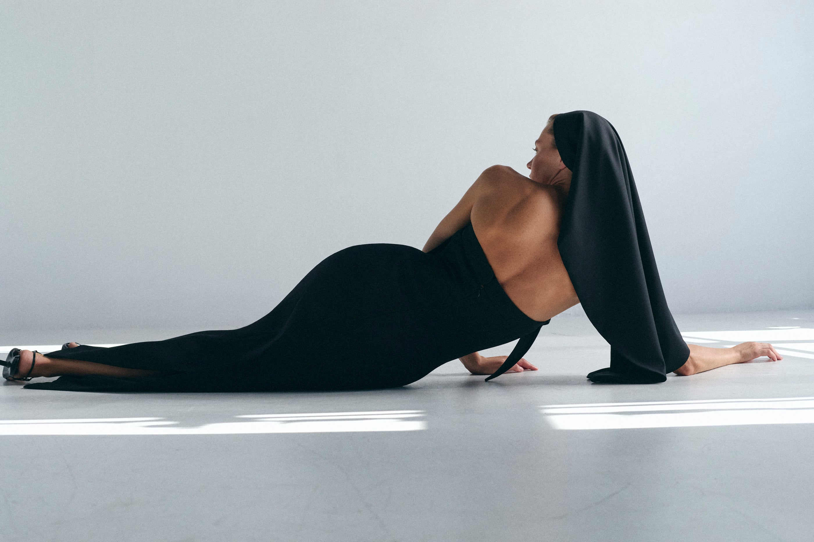 Woman in a black dress lying on a white floor against a white wall