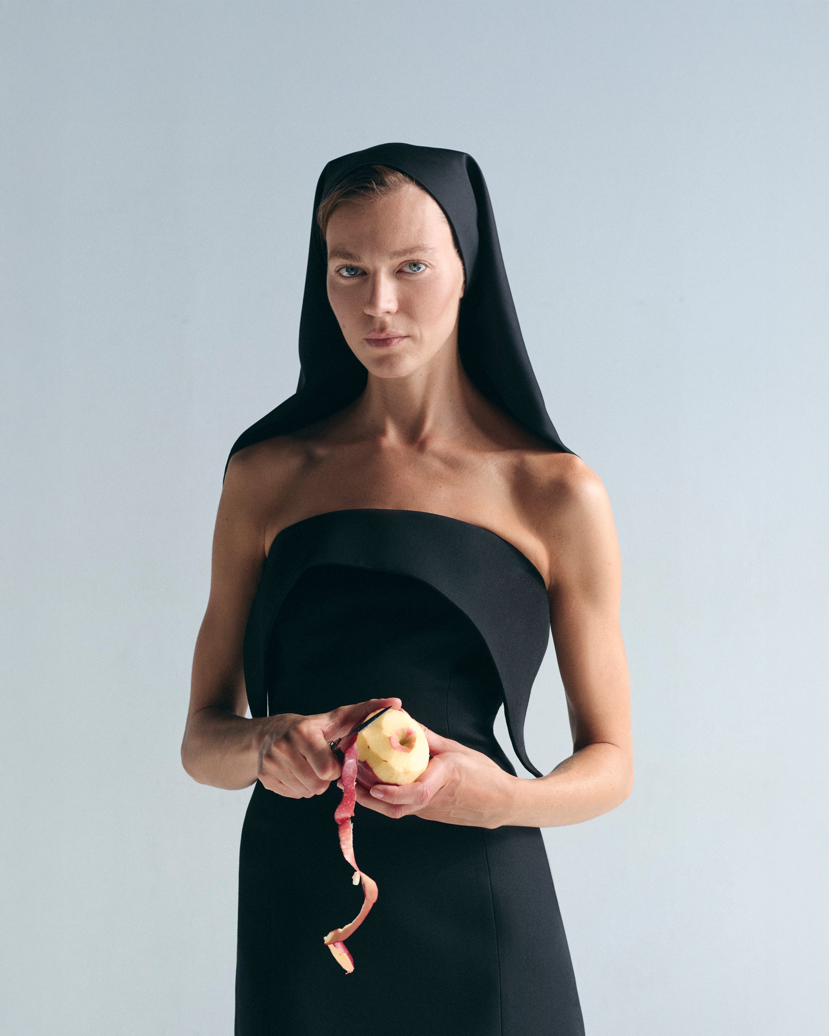 Woman in a black dress holding an apple against a plain background