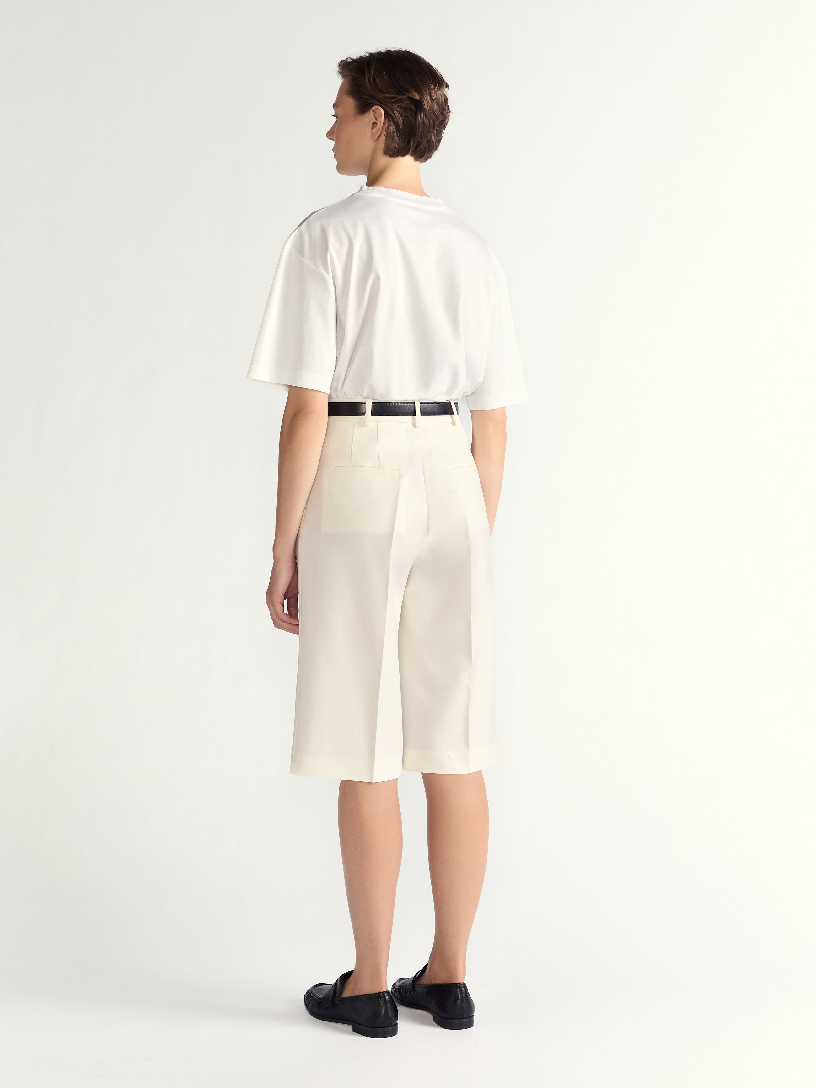 Person wearing a white shirt and ivory shorts on a plain background