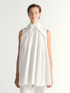 Person wearing a white sleeveless dress with a high collar on a plain background