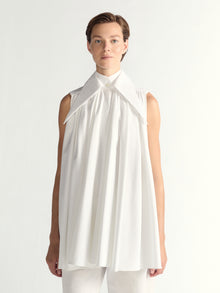 Person wearing a white sleeveless dress with a high collar on a plain background