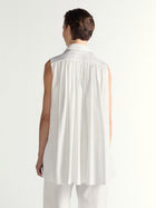 Person wearing a sleeveless white dress on a plain background