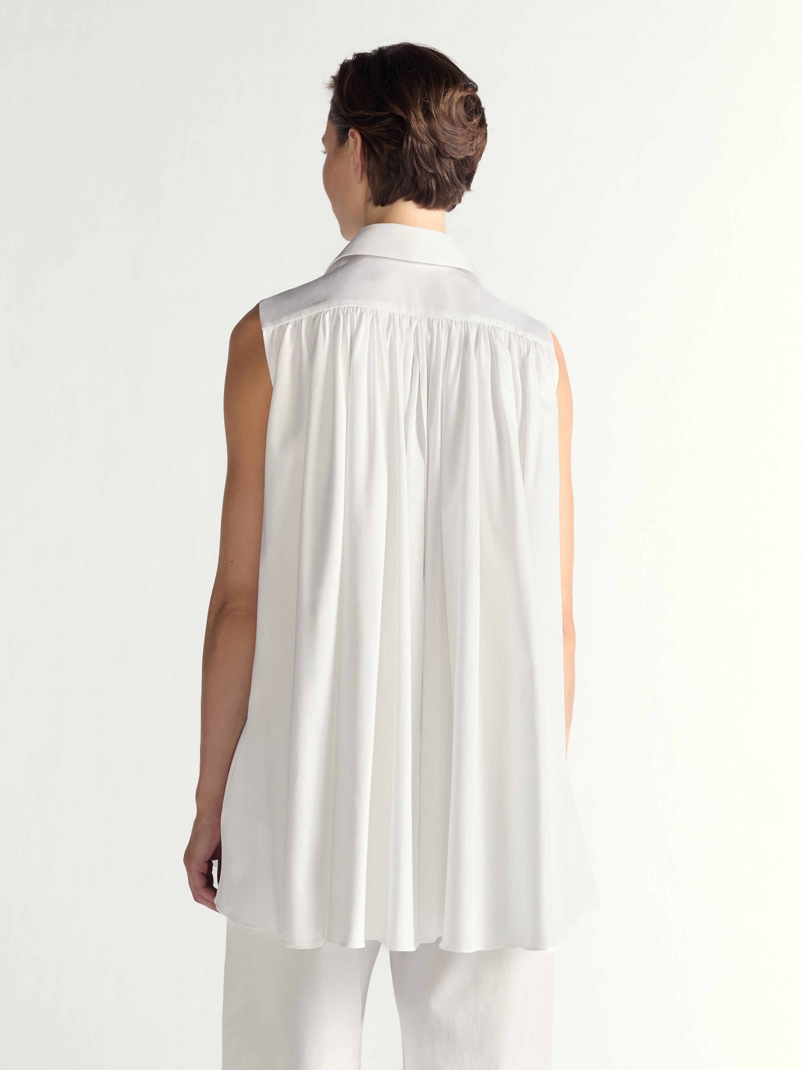 Person wearing a sleeveless white dress on a plain background